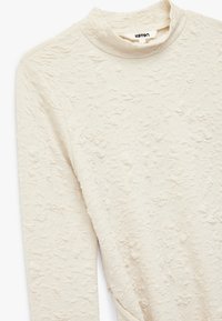 Cremefarvet langærmet struktureret bluse med et subtilt præget blomster mønster og en lille mock neck krave.