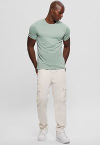Camiseta ajustada de color verde menta con mangas cortas, combinada con pantalones cargo de color beige claro que tienen bolsillos laterales y zapatillas blancas.