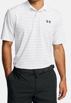 Mężczyzna w białej koszulce polo z krótkim rękawem z cienkimi czarnymi poziomymi paskami, czarnym logo Under Armour, czarnym plecionym paskiem i czarnymi spodniami.