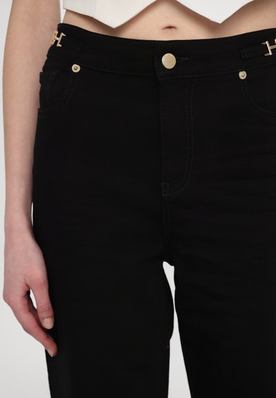 Black denim jeans with a fitted design, featuring gold hardware accents, a front button closure, and contrasting stitching details.