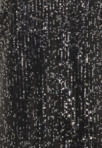 Tela negra cubierta de brillantes lentejuelas plateadas, que muestra una superficie texturizada con tamaños variados y una disposición densa.