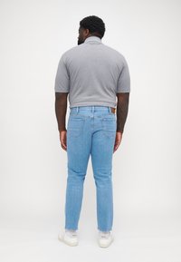 Polo grigio a maniche corte, abbinato a jeans in denim azzurro chiaro e sneakers bianche. Tasche posteriori visibili sui jeans.