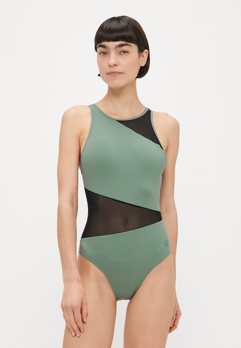 Ολόσωμο μαγιό σε ελιά πράσινο με μαύρες διακοσμήσεις από δίχτυ. Διαθέτει ψηλό λαιμό, κομψό σχέδιο και λείο υφή.