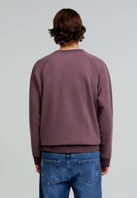 Felpa viola con maniche raglan, polsini e orlo a costine, abbinata a jeans di denim blu con due tasche posteriori.