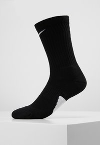 Mustad mustreeritud mustad spordisokid, keskmise säärekõrgusega, tugevdatud varbakohaga ja valge logoga külgedel; sokil on kontrastne valge kand.