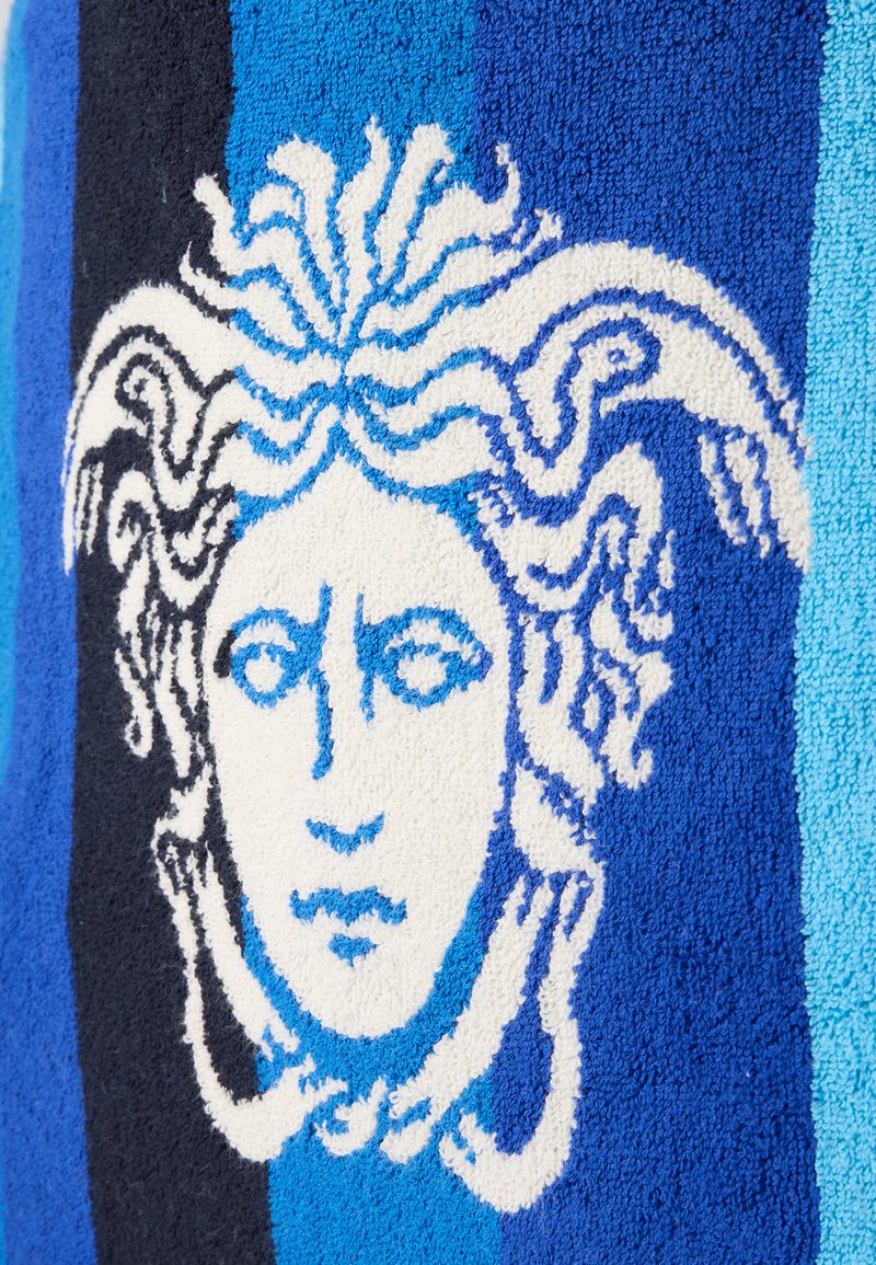 Design tête de Méduse blanc et bleu sur un fond en tissu à rayures bleu et noir texturé.
