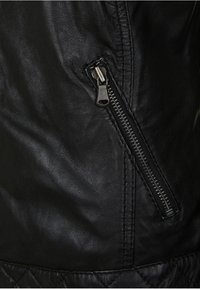 Black leather jacket detail featuring a side zipper, textured surface, and visible stitching along the seams. Quilted pattern at the bottom.