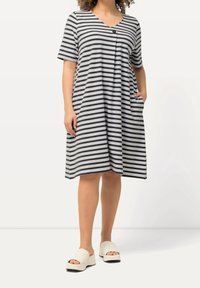 Pasiasta, szaro-biała sukienka z krótkim rękawem, dekoltem w serek, detalami guzika, kieszeniami i luźnym krojem. Noszona z jasnokolorowymi sandałami na platformie.