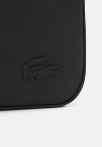 Borsa nera con texture, caratterizzata da un logo impresso in evidenza, con un bordo morbido e curvo e un design minimalista.