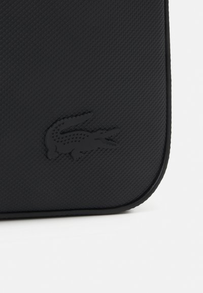 Sac noir texturé avec un logo en relief bien en vue, doté d'un bord courbé lisse et d'un design minimaliste.