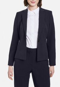 Navyblazer mit taillierter Passform, strukturierten Schultern, einer Ein-Knopf-Verschluss und zwei vorderen Taschen. Kombiniert mit einem weißen Hemd mit Kragen.