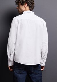 Wit overhemd met lange mouwen en een textuurafwerking, casual ontwerp, knoopmanchetten en een licht gebogen zoom, gedragen met donkerblauwe jeans.