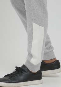 Gray sweatpants with a white fabric panel on the side, paired with black sneakers featuring a textured surface and white sole.