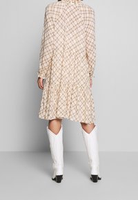 Beige, patterned long-sleeve dress with ruffled hem; paired with white cowboy boots featuring a pointed toe and block heel.