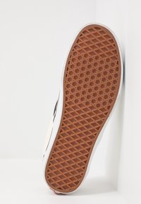 Suela de zapato con una superficie de goma estampada en marrón, que presenta un diseño de cuadrícula texturizada. Los bordes son blancos con una ligera curvatura.