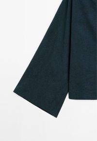 Tma zelená látka s jemným texturovaným vzorem připomínajícím plynulé linie. Spodní okraj je rovný s mírným úhlovým střihem.