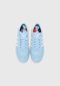 Lyseblå sneakers laget av glatt lær, med tre hvite striper, vingspissdesign og en kontrasterende mønstret såle.
