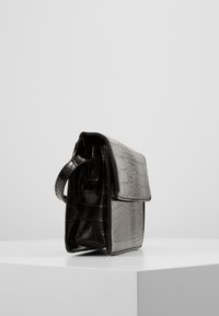 Borsa in pelle stampata a coccodrillo grigia e nera, forma strutturata, chiusura a soffietto e una sola tracolla. Texture liscia con un motivo sottile.