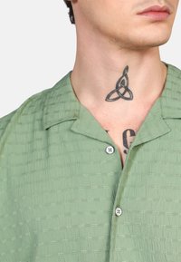 Camisa de manga corta verde claro con un patrón tejido texturizado, cuello con solapa y dos botones en la parte frontal.