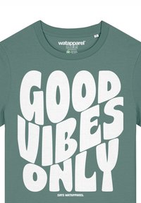 Groene katoenen T-shirt met een ronde hals. Kenmerkt zich door vet witte letters: "GOEDE VIBES ALLEEN," met een speelse letterstijl en een gladde textuur.