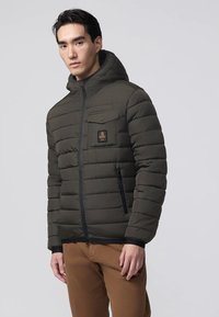 Giacca imbottita con cappuccio di colore verde scuro, caratterizzata da una trapuntatura orizzontale, una tasca con zip e una toppa con logo sul petto. Chiusura semplice con zip e polsini.