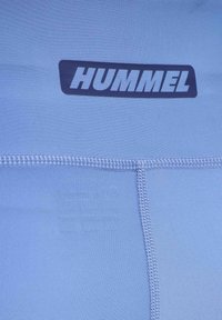 Tissu bleu avec coutures visibles et un logo HUMMEL noir imprimé près du centre supérieur du matériau.