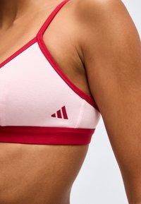 Κοντινό πλάνο ενός ατόμου που φοράει ροζ και κόκκινο αθλητικό σουτιέν με ένα μικρό σκουροκόκκινο τρίγωνο λογότυπο στο πλάι.