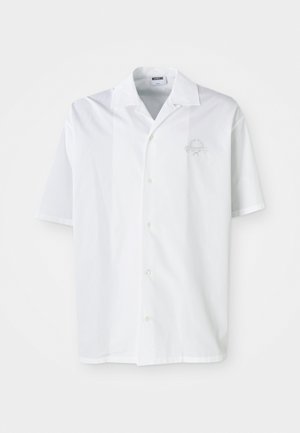 Chemise blanche à manches courtes avec un col pointu, fermeture à boutons et un design brodé sur la poitrine gauche. Texture de tissu lisse.