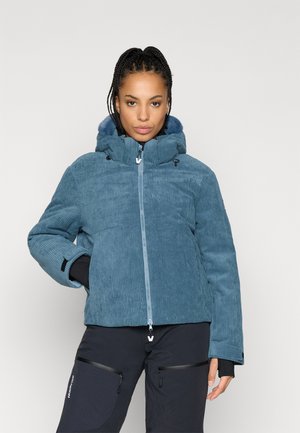 Chaqueta con capucha de pana azul con cierre de cremallera, con un acabado texturizado y puños elásticos, combinada con pantalones negros.