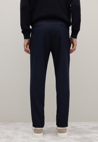 Marineblaue Hose mit geradem Schnitt aus weichem Stoff, mit Gesäßtaschen, kombiniert mit hellen Sneakers auf einer strukturierten Oberfläche.