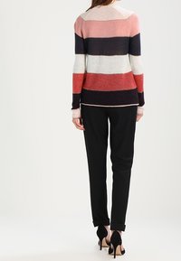 Gestreepte trui in roze, crème, marineblauw en rode tinten; zacht gebreide textuur; gecombineerd met zwarte broek en hoge hakken.