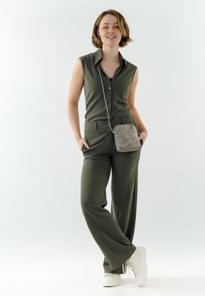 Olijfgroene, mouwloze knoopblouse en bijpassende wijde broek. Geaccentueerd met een kleine, gestructureerde grijze schoudertas en witte sneakers.