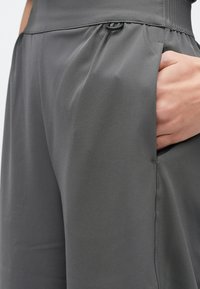 Szürke nadrág sima anyagból, laza szabással, rugalmas derékrésszel és oldalzsebbel, látható textúrájú anyaggal.