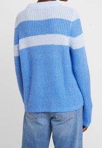 Pull en maille avec larges rayures horizontales bleu clair, bleu foncé et blanc. Coupe décontractée, encolure ronde, texture côtelée.