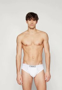 Fehér Versace alsónadrág sima anyagból, fekete logós derékszíjjal. A dizájn egyszerű, további minták vagy díszítések nélkül.