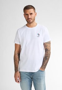 Bílá bavlněná tričko s kulatým výstřihem a krátkými rukávy, se malým vyšitým palmou v barvách na levé části hrudi.