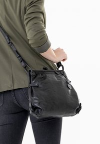 Borsa a mano in pelle nera con una finitura morbida e strutturata, caratterizzata da bordi arrotondati, una tracolla e dettagli in metallo.