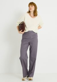 Suéter de punto beige claro con un escote amplio, combinado con pantalones de cintura alta de rayas moradas y zapatillas beige y marrón.