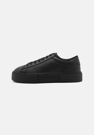 Zapatilla negra de corte bajo con suela gruesa, cierre de cordones en la parte delantera y discreto logotipo "Tommy Jeans" en la entresuela lateral.