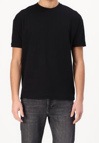 Černé bavlněné tričko s kulatým výstřihem. Krátké, ohrnuté rukávy a volný střih. V kombinaci s tmavě šedými džínami.