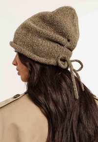 Cappello di maglia marrone con punta, dotato di un dettaglio annodato sul retro e realizzato in un materiale caldo e testurizzato.