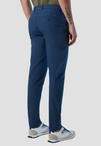 Chino blu navy con una texture liscia, gambe affusolate e tasche posteriori con bottone, abbinati a scarpe da ginnastica bianche e grigie.