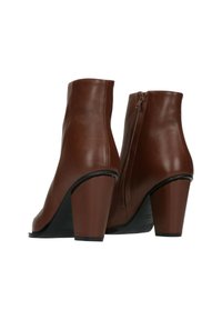 Un paio di stivali in pelle marroni alla caviglia con tacco a blocco e cerniere laterali, mostrati da una vista posteriore a tre quarti su uno sfondo bianco.