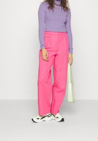 Klart rosa vida byxor med en mjuk textur, kombinerat med en figurnära lavendelfärgad höghalser. Svart och vit sneakers. Ljust grön handväska.