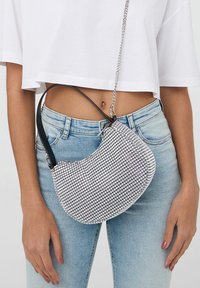 Borsa a spalla a scacchi in bianco e nero con un design curvo, manici in catena e pelle, tessuto testurizzato e forma compatta.