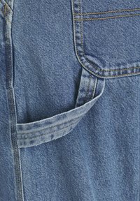 Tejido de mezclilla azul con un detalle de bolsillo, que presenta costuras amarillas en contraste y un acento de tela en bucle. Textura suave, tono azul estándar.