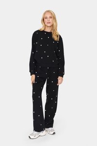 Set di felpa e pantaloni neri con motivi a cuore bianchi sparsi. Tessuto morbido, vestibilità rilassata, scollatura rotonda e polsini e vita elastici.