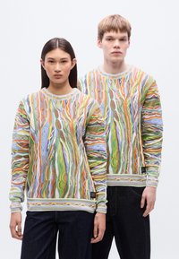 Χρωματιστά πλεκτά φούτερ με περίπλοκα σχέδια από κυματιστές, αφηρημένες γραμμές σε πράσινο, πορτοκαλί, μπλε και κίτρινο σε  ανοιχτό φόντο.