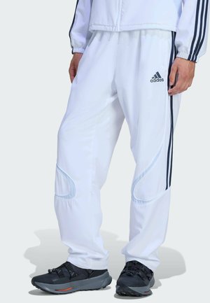 Witte sportieve broek met zwarte zijstrepen en accenten, gemaakt van lichtgewicht materiaal met een gladde textuur en een taps toelopende pasvorm.