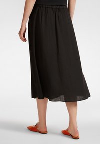 Gonna midi in lino nera con vita elastica, caratterizzata da una vestibilità morbida e una texture liscia. Indossata con scarpe arancioni slip-on.